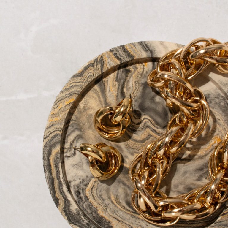 Goldene Kette und Ohrringe auf einer marmorierten Platte.